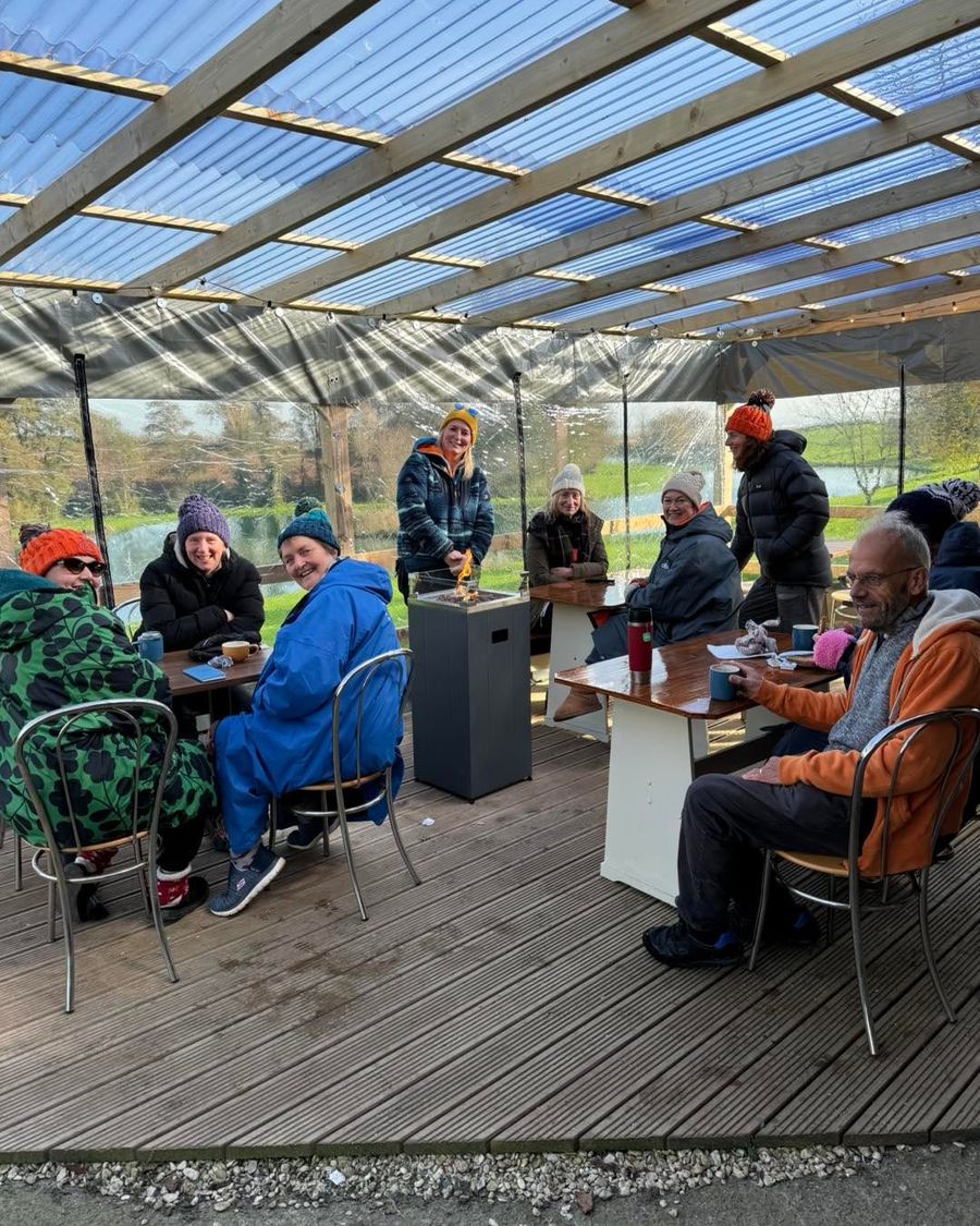 Swimmers at the tables under the covered decking with the lake behind, Court Farm Lakes