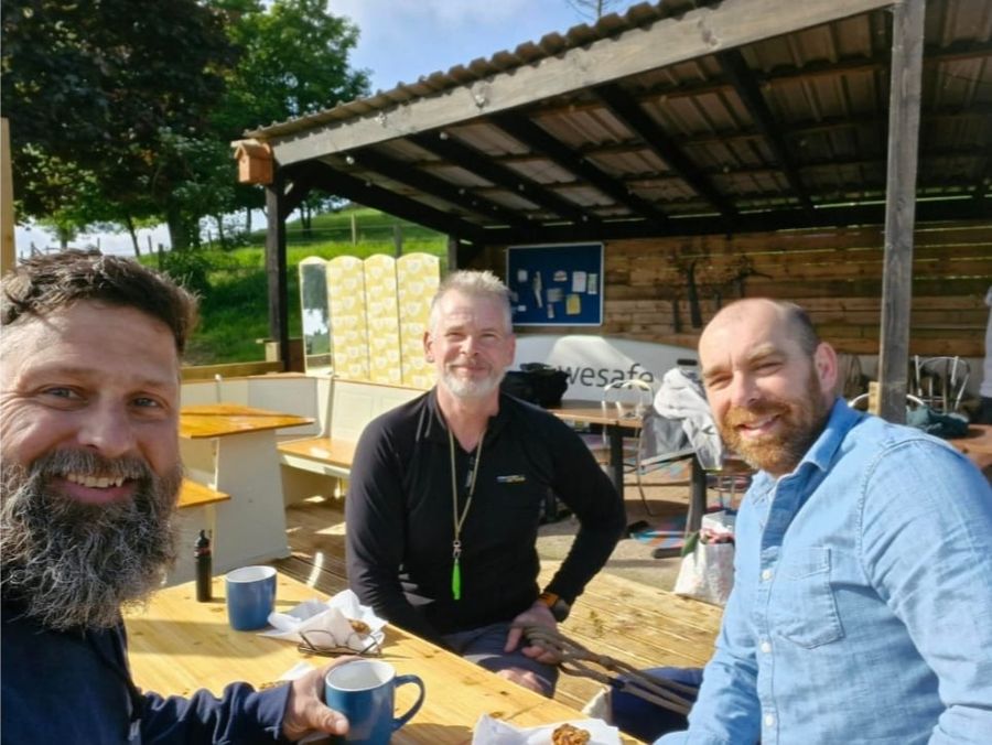 Three swimmers with mugs at the outdoor table after a swim, Court Farm Lakes