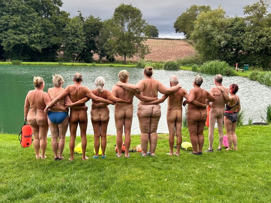 The clothing optional swimmers arm in arm on the bank, looking out over the lake, Court Farm Lakes