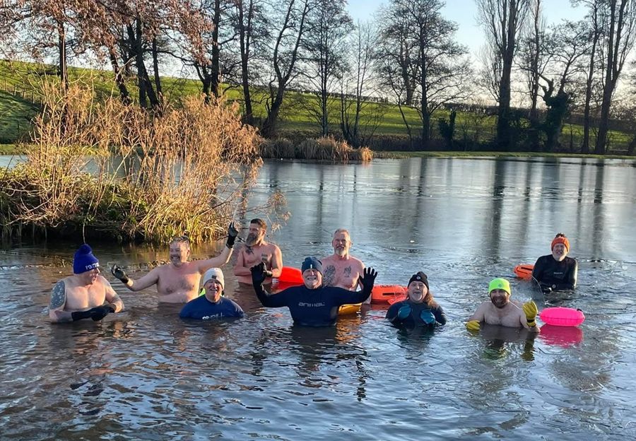 A winter swim group in bobble hats waving from the lake, Court Farm Lakes
