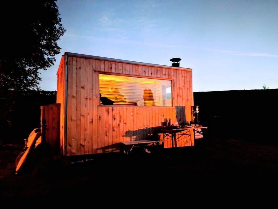 The wood-fired sauna cabin on the bank of the lake at dusk, its deck lit, Court Farm Lakes